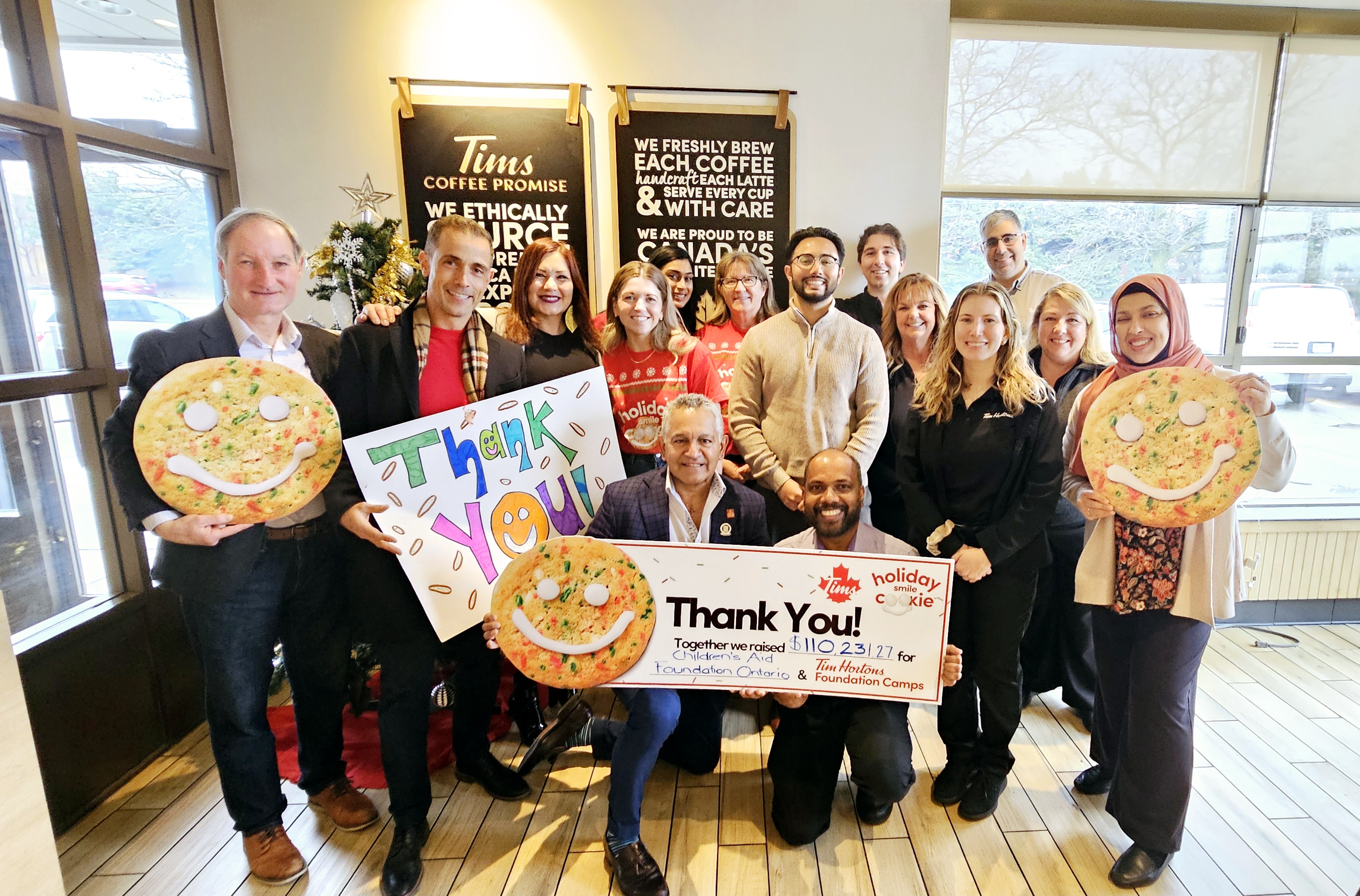 Group photo of staff and board members holding large cheque and giant smile cookies and thank you sign.